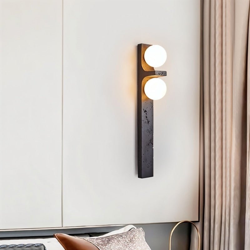 Clérachic black stone-effect wall lamp with two warm globes above a bed, beside a soft taupe curtain.