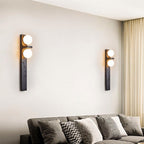 Two Clérachic black wall lamps with frosted globes hung on a pale living room wall above a grey sofa and cushions.