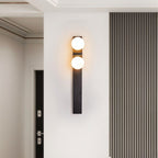 Clérachic black wall lamp with two warm glass globes in a hallway, beside a ribbed grey wall panel and a dark door.
