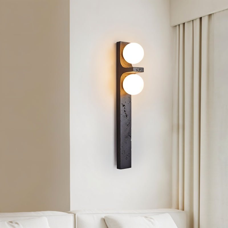 Clérachic black stone-effect wall lamp with two lit globes beside cream curtains and a white sofa, casting a warm glow.
