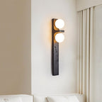 Clérachic black stone-effect wall lamp with two lit globes beside cream curtains and a white sofa, casting a warm glow.