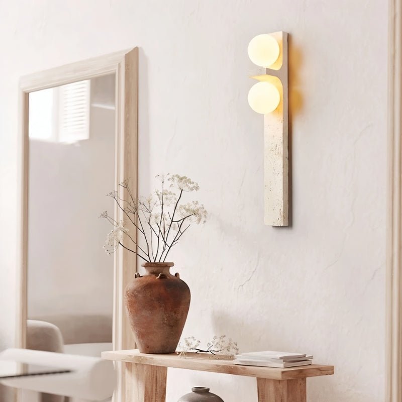 Clérachic travertine wall lamp on textured plaster above a rustic console with a terracotta vase and dried flowers.
