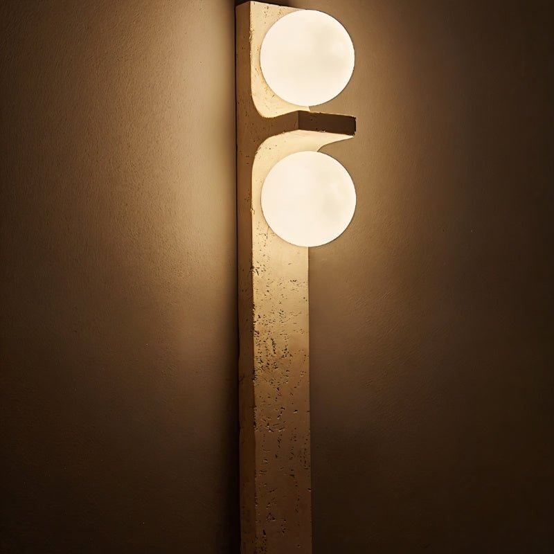 Close view of a Clérachic travertine wall lamp lit in a dim room, its pitted cream stone and two soft globes glowing.