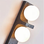 Close-up of the Clérachic black wall lamp, speckled stone-effect surface and two bright frosted globes on a pale wall.