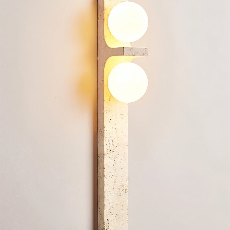 Clérachic travertine wall lamp seen at a slight distance, two lit globes above a long, softly veined cream stone bar.