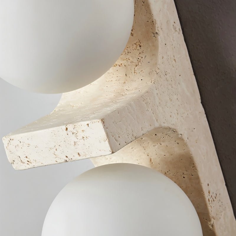 Macro of the Clérachic travertine wall lamp showing the porous cream stone ledge and two matt white glass globes.