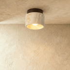 Clérachic short travertine ceiling light with a dark walnut canopy, the bulb lit warm inside the stone cylinder.