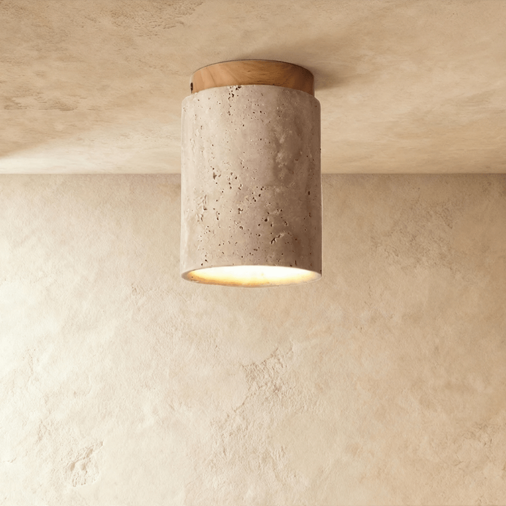 Clérachic tall travertine cylinder ceiling light with a light wood canopy, pitted stone surface and a soft glow below.