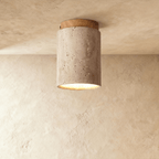 Clérachic tall travertine cylinder ceiling light with a light wood canopy, pitted stone surface and a soft glow below.