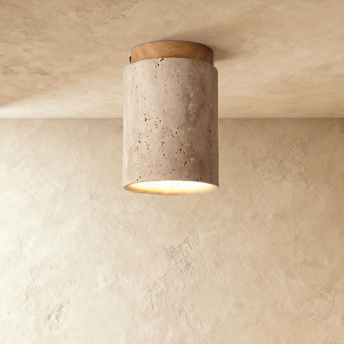 Clérachic tall travertine cylinder ceiling light with a light wood canopy, pitted stone surface and a soft glow below.