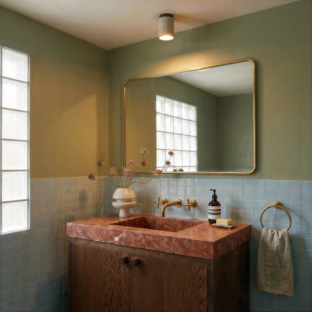 Clérachic tall travertine ceiling light above a green-tiled bathroom vanity with a brass-framed mirror and pink stone basin.