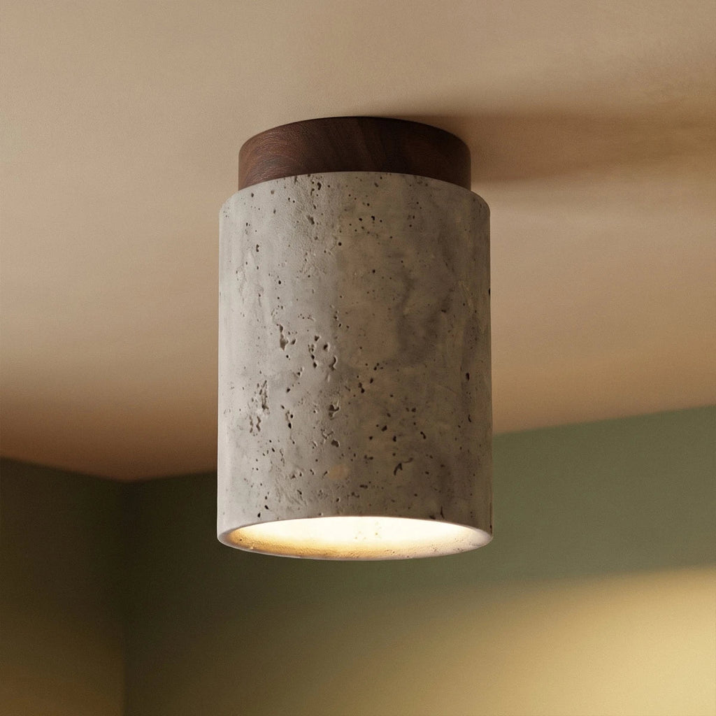 Close view of a Clérachic tall travertine ceiling light, walnut wood canopy and pitted stone against a green wall corner.