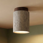 Close view of a Clérachic tall travertine ceiling light, walnut wood canopy and pitted stone against a green wall corner.
