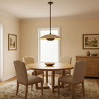 A flat Clérachic travertine pendant hangs above a round wooden dining table with upholstered chairs in a cream room.