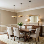 Three Clérachic travertine pendants hang in a row above a long dark dining table, with a mirror and table lamps behind.