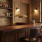 A Clérachic pendant glows over a dark wood bar counter, with bottles on shelves and brick wall lights behind.