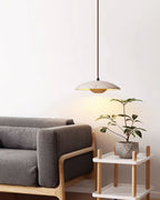 A small Clérachic travertine pendant hangs above a grey sofa and a potted plant on a white side table.