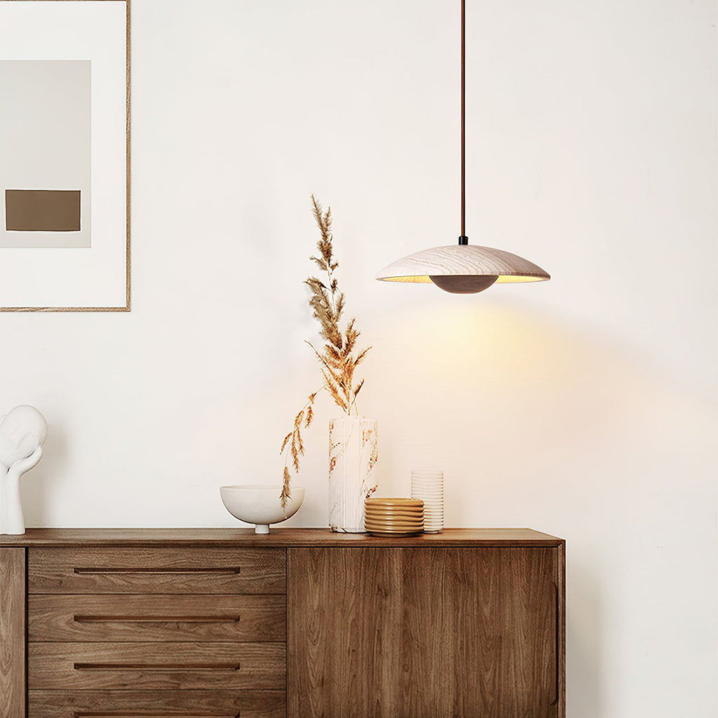 A Clérachic pendant with a travertine shade hangs beside a walnut sideboard with dried stems and a framed print.