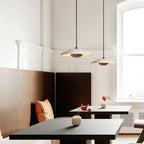 Two Clérachic pendants with stone shades hang above dark tables and a leather banquette in a bright, panelled room.