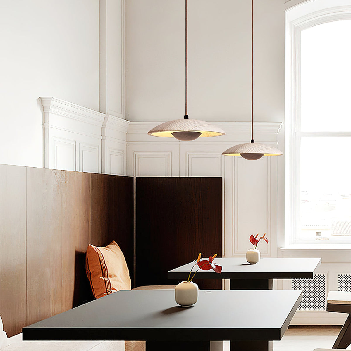 Two Clérachic pendants with stone shades hang above dark tables and a leather banquette in a bright, panelled room.