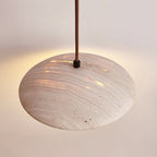 Seen from the side, the rounded travertine shade of this Clérachic pendant glows through its pores in warm light.