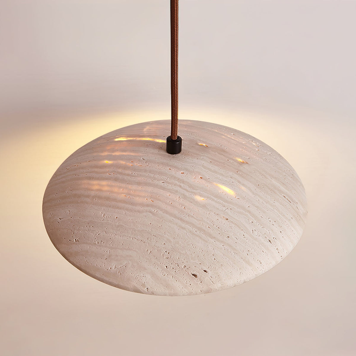Seen from the side, the rounded travertine shade of this Clérachic pendant glows through its pores in warm light.