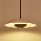 Underside view of a Clérachic pendant, with a rim of warm light around the stone shade and a dark bowl in the middle.