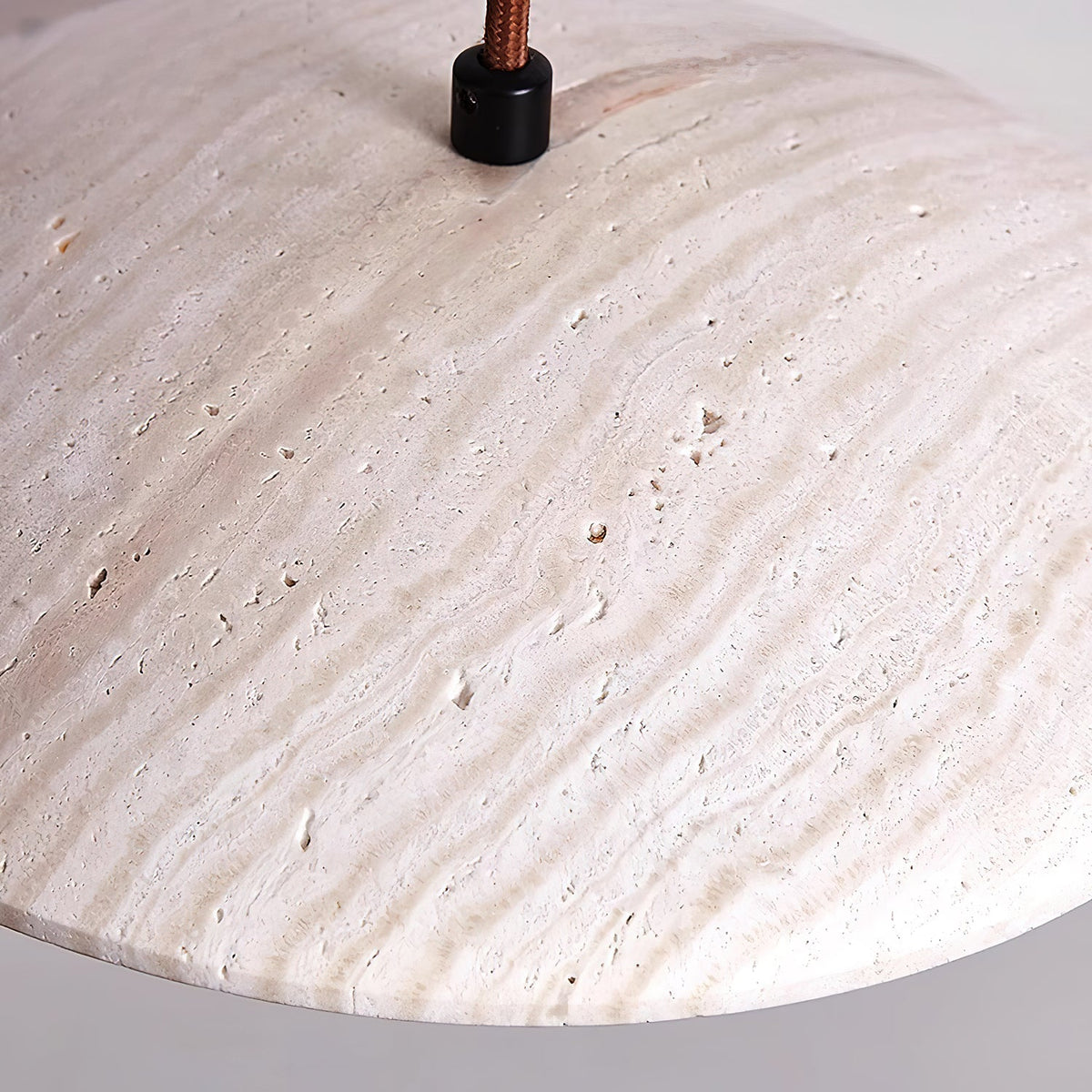 Close view of the veined surface and fabric cord entry at the top of this Clérachic pendant's travertine shade.