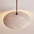 Side view of the rounded travertine shade of this Clérachic pendant, with warm light showing through the pores.