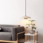 This Clérachic pendant hangs by a grey sofa with a potted plant on a white side table, its warm glow on the wall.