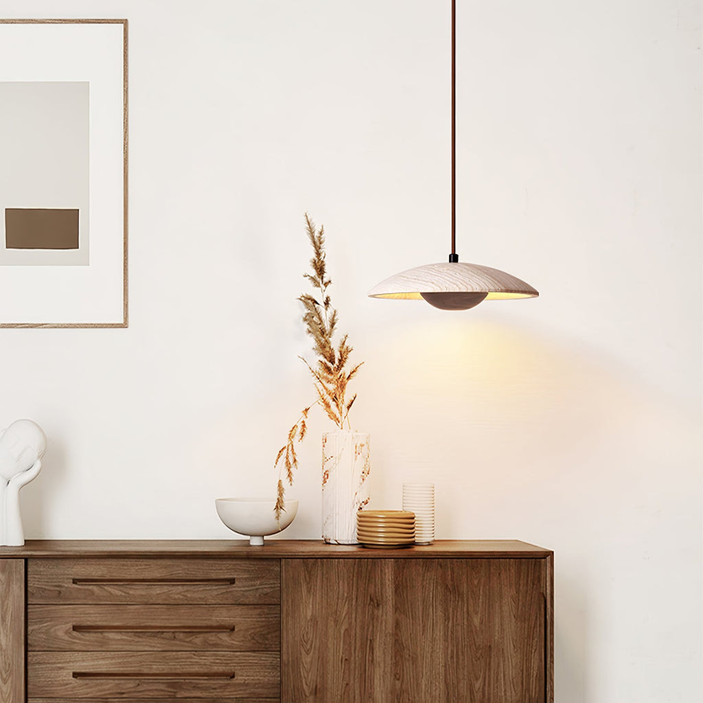 A Clérachic travertine pendant glows above a walnut sideboard with a pale bowl, dried grasses and a framed print.