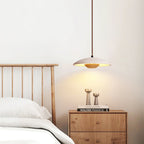 Above a slatted headboard and a wooden bedside chest, the stone shade of this Clérachic pendant glows warm.