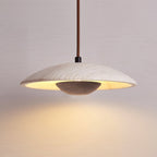A Clérachic pendant with a dark walnut-toned bowl under a travertine shade hangs against a soft mauve-grey wall.