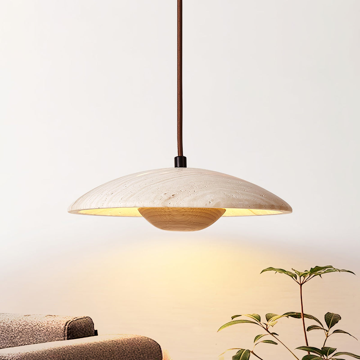 Close shot of this Clérachic pendant, travertine shade above a light wood bowl, lit warm against a pale wall.