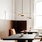 Two Clérachic pendants hang above a leather banquette and black tables in a room with a tall arched window.