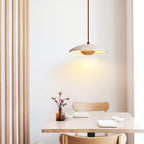 A Clérachic travertine pendant hangs above a small table with a vase of buds and a pale wooden chair.