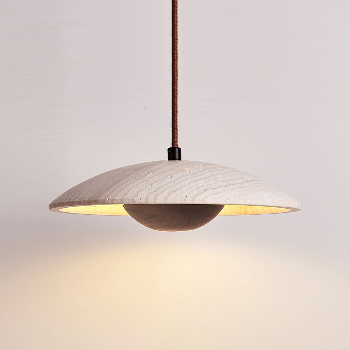 This Clérachic pendant with a dark walnut-toned bowl glows warm from beneath its wide travertine shade.