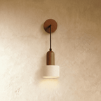 Clérachic wall lamp with a round wooden backplate, thin arm and a cylindrical speckled travertine shade, lit on limewash.