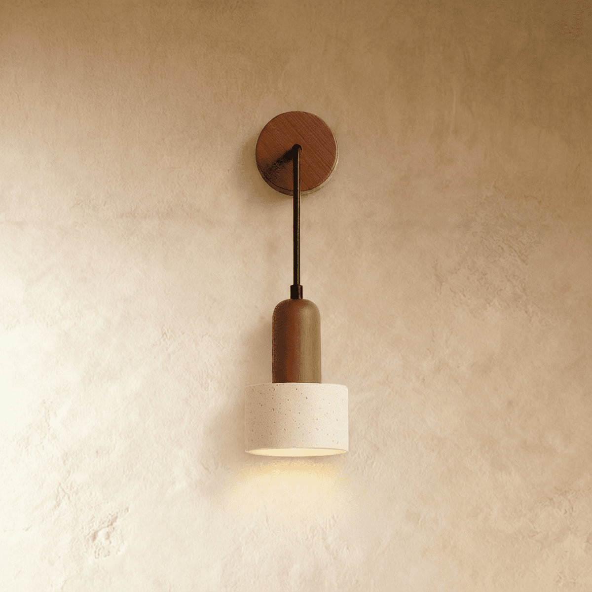 Clérachic wall lamp with a round wooden backplate, thin arm and a cylindrical speckled travertine shade, lit on limewash.