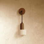 Clérachic wall lamp with a wood backplate, bronze-toned stem and a cylindrical travertine shade on a warm plaster wall.