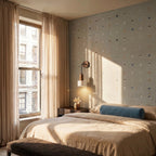 Clérachic wall lamp with a travertine cylinder shade lit above a bedside table in a sunlit bedroom with linen curtains.