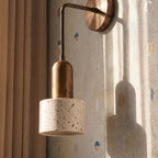 Close view of the Clérachic wall lamp, a bronze-toned arm and stem above a speckled travertine cylinder shade.