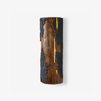 Tall half-round Clérachic wall light in the Bark finish, with a warm glow showing through a slit in its brown and blue-grey textured surface.