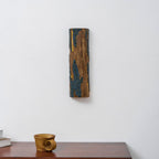 A Clérachic Bark wall light hangs on a white wall above a dark wood sideboard holding a small wooden cup and a stack of books.
