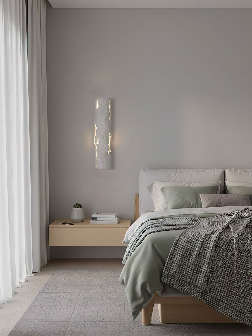 Seen across a calm bedroom, a white Clérachic wall light glows through its fine cracks above a pale wood bedside table.