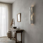 A white Clérachic wall light with a rough plaster-like surface lights up its cracks on a limewashed wall above a rustic console table.