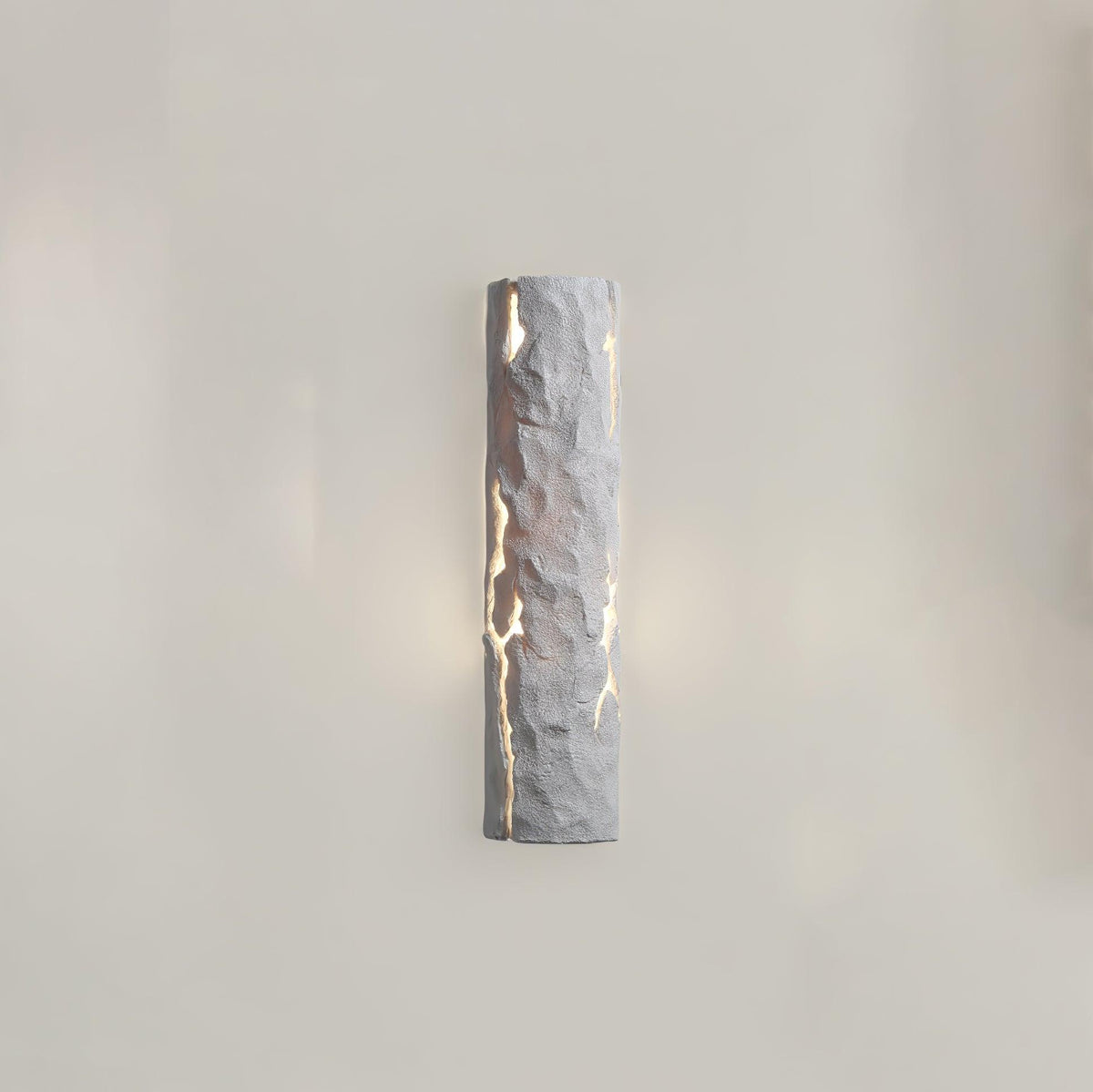 Straight-on view of a white Clérachic wall light with a hand-chiselled look, its cracks glowing and a soft halo on the wall behind.