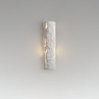 A white Clérachic wall light on a grey gradient backdrop, with a soft halo of warm light on either side of its cracked surface.