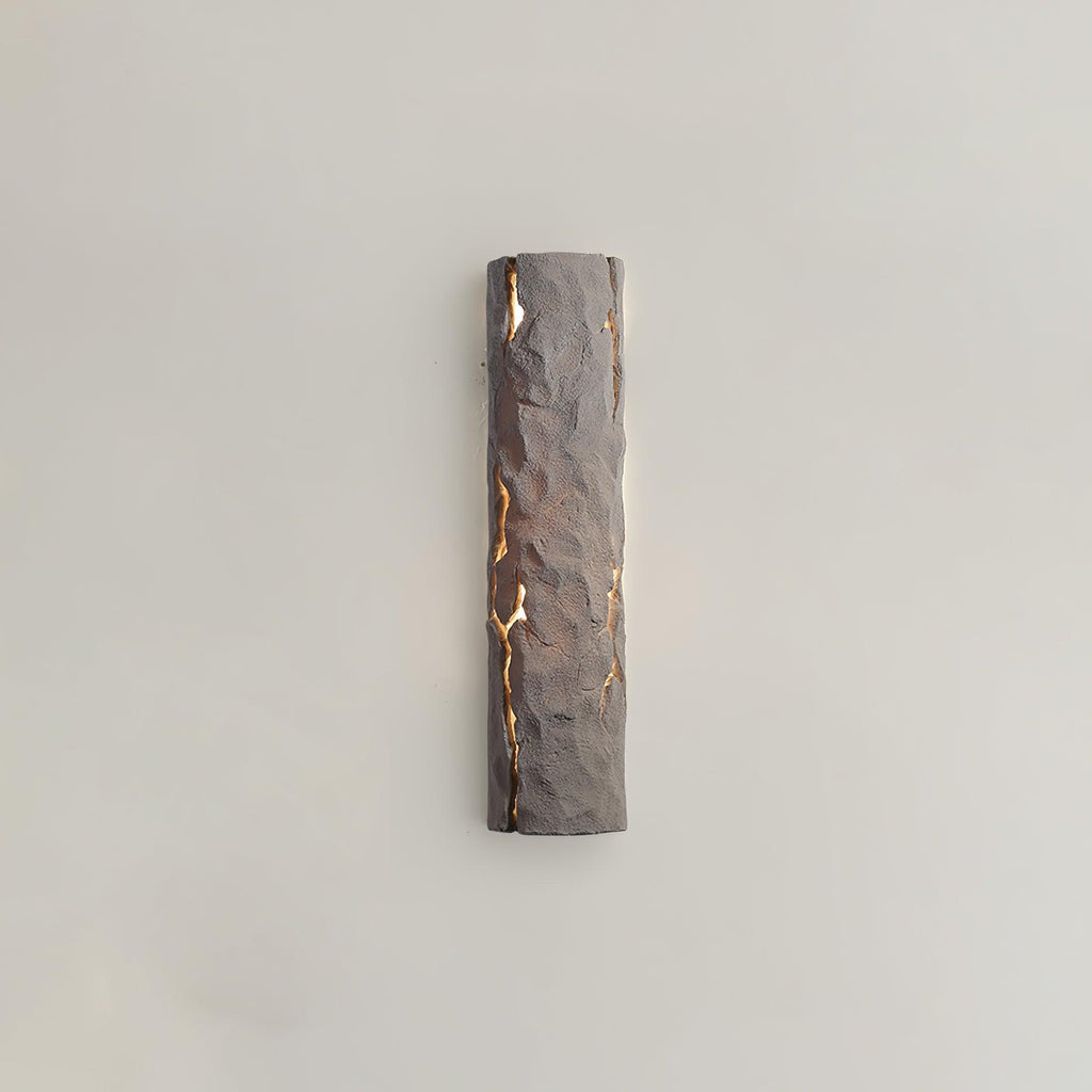 A taupe-toned version of this Clérachic wall light, its chiselled surface lit through cracks, on a warm greige wall.