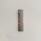 A taupe-toned version of this Clérachic wall light, its chiselled surface lit through cracks, on a warm greige wall.